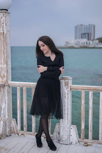 Morena chica en un vestido negro posando en el muelle —  Fotos de Stock