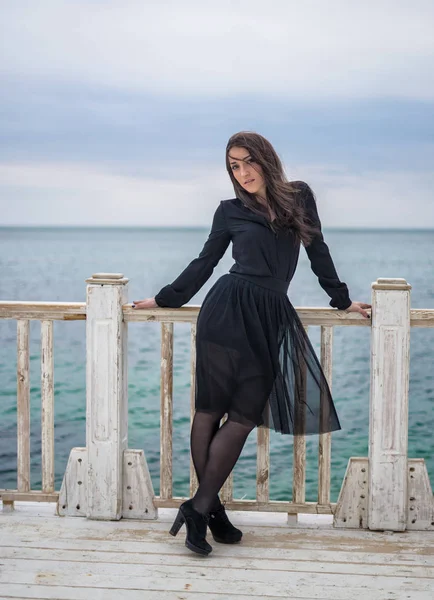 Brunett flicka i en svart klänning som poserar på piren — Stockfoto