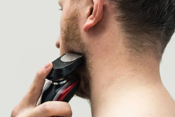 young man shaving his beard off with an electric shaver