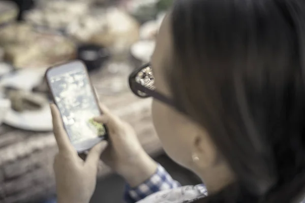 Chica inteligente con gafas usando el teléfono móvil mientras come — Foto de Stock