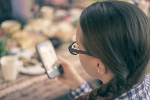 Chica inteligente con gafas usando el teléfono móvil mientras come — Foto de Stock