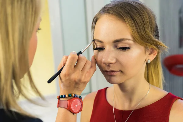 Make-up artist doing makeup to beautiful young girl