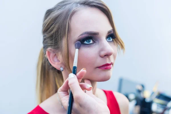 Make-up artist doing smoky eyes makeup to beautiful young girl — Stok Foto