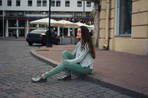 Vacker flicka sitter på en stadsgata på stävja och ser fram. — Stockfoto