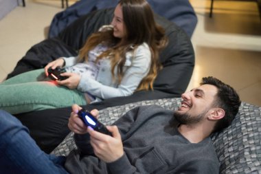 Fasulye çanta sandalyede oturan joystick ile video oyunları oynarken mutlu çift arkadaş