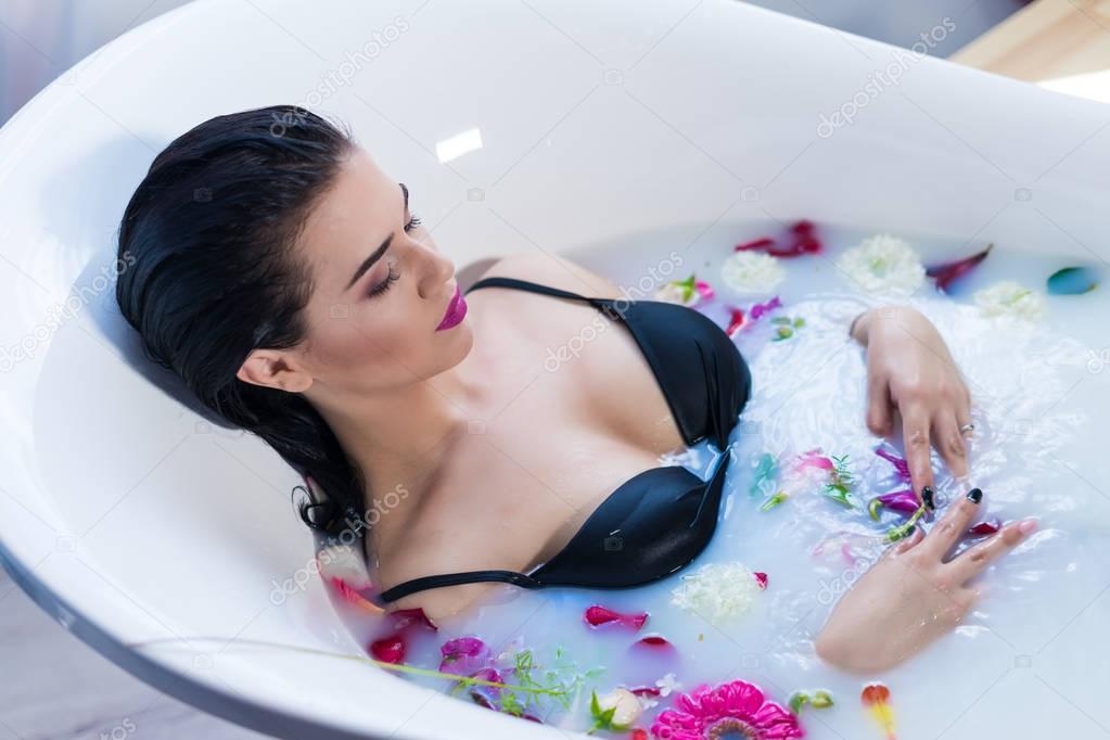 Sexy brunette woman taking a hot bath with flowers