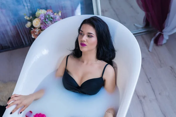 Sexy donna bruna rilassante nel bagno di latte caldo con fiori — Foto Stock