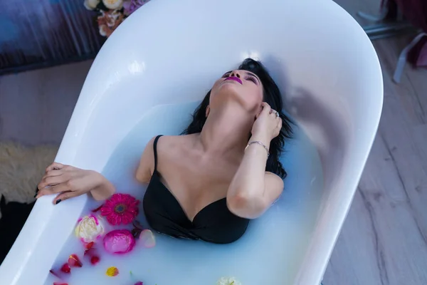 Sexy brunette woman relaxing in hot milk bath with flowers — Stock Photo, Image