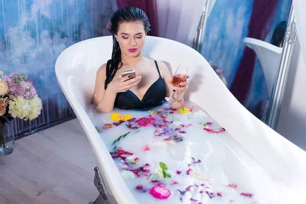 Sexy bruna donna è seduta in bagno e chatta su smartphone — Foto Stock
