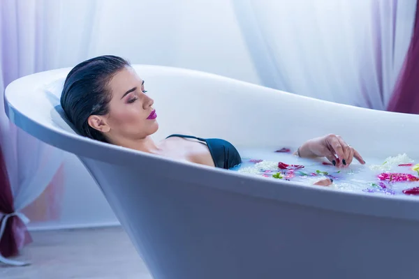 Sexy brunette woman relaxing in a hot bath with flowers — Stock Photo, Image