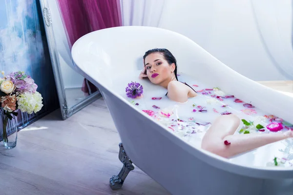 Sexy brunette woman relaxing in a hot bath with flowers — Stock Photo, Image
