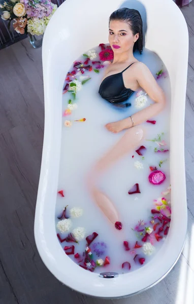 Sexy brunette woman relaxing in hot milk bath with flowers — Stock Photo, Image