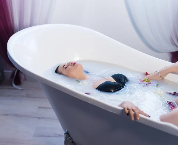 Sexy donna bruna rilassante nel bagno di latte caldo con fiori — Foto Stock