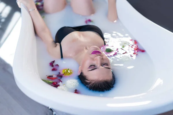 Sexy brunette woman relaxing in hot milk bath with flowers