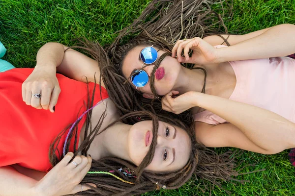 Duas amigas com cornrows zizi dreadlocks deitado no gramado verde — Fotografia de Stock