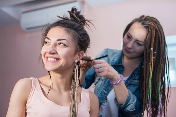 Un estilista de pelo trenzas hileras de maíz Zizi a una joven y hermosa chica — Foto de Stock