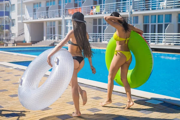 Две сексуальные хипстерки танцуют с кругами в бассейне — стоковое фото
