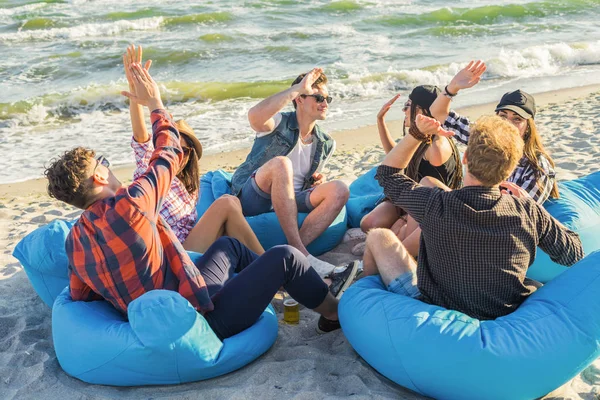 group of friends giving high five on beach sitting on bean bags