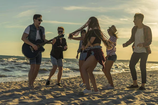 快乐的朋友们在沙滩上跳舞。男人弹吉他 — 图库照片