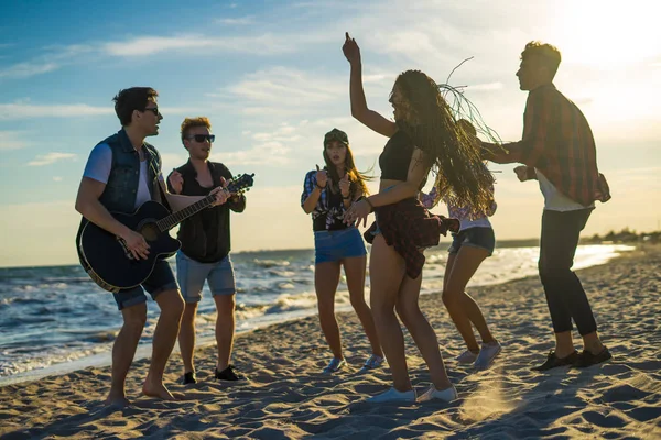Amigos felizes dançando na praia. Homens estão tocando guitarra — Fotografia de Stock