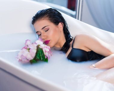 Seksi esmer kadın çiçekler ile sıcak bir banyoda rahatlatıcı
