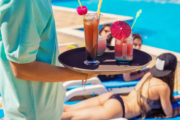 Waiter brings colorful cocktails to young sexy girls for a party in the pool — Stock Photo, Image