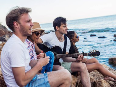 taşlar sahilde oturan arkadaşlar. adam gitar çalıyor.
