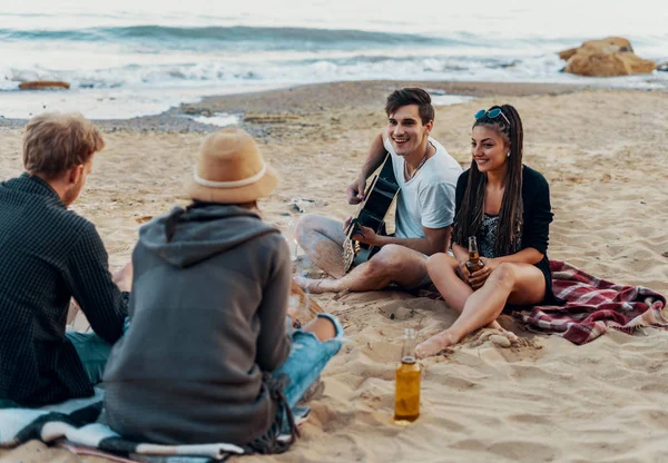 Freunde sitzen auf Steinen am Strand. Mann spielt Gitarre. — Stockfoto