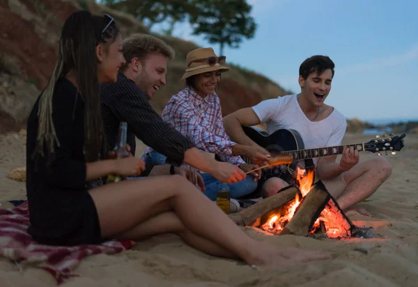 Freunde sitzen am Strand. Mann spielt Gitarre. — Stockfoto