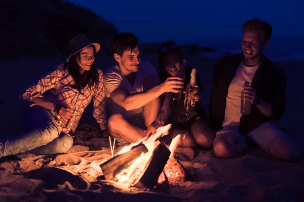 Amigos sentados en la playa clink vasos cerca de la hoguera — Foto de Stock