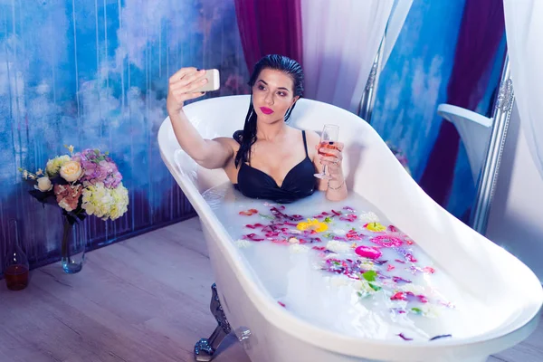 Sexy brunette woman shooting selfie having a hot milk bath with flowers — Stock Photo, Image