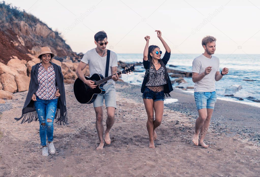 group of young and cheerful friends walking on beach