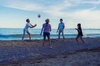 günbatımı sırasında vahşi bir sahilde voleybol oynarken arkadaşlar