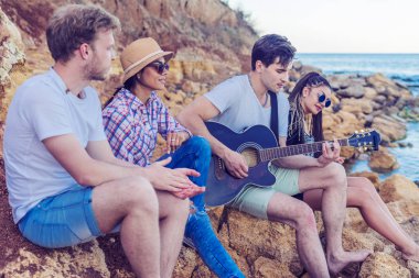 taşlar sahilde oturan arkadaşlar. adam gitar çalıyor.