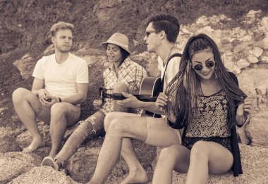 taşlar sahilde oturan arkadaşlar. adam gitar çalıyor.