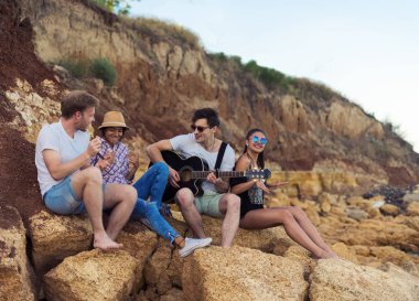 taşlar sahilde oturan arkadaşlar. adam gitar çalıyor.