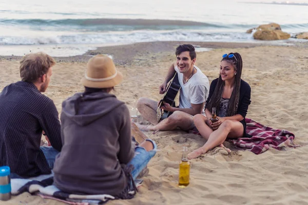 Amigos sentados em pedras na praia. homem está tocando guitarra . — Fotografia de Stock