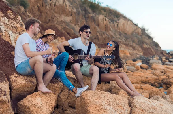 Друзі сидять на камені на пляжі. людина грає на гітарі . — стокове фото