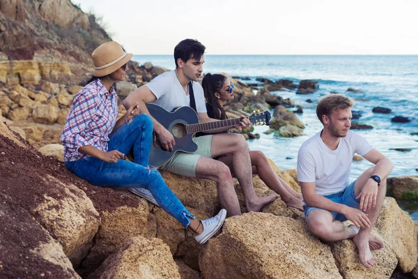 taşlar sahilde oturan arkadaşlar. adam gitar çalıyor.