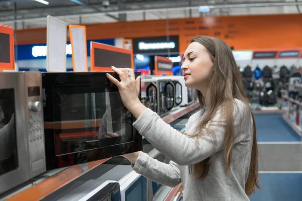 Chica cliente elige un horno de microondas en una tienda de electrodomésticos — Foto de Stock