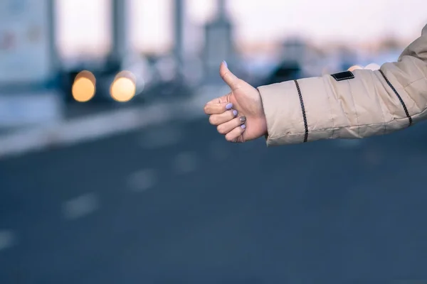 Mano de mujer autoestopista chica con luces borrosas y la ciudad en el fondo . — Foto de Stock