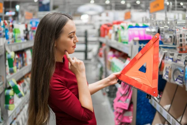 Joven conductor femenino compra triángulo de advertencia en el departamento de automóviles de supermercado . — Foto de Stock