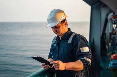 Güverte görevlisi offshore gemi veya gemi güvertede, PPE kişisel koruyucu ekipman giyiyor. Kontrol listesini doldurur. Denizdeki evraklar