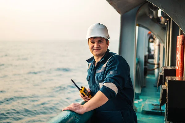 Oficial de convés marinho ou companheiro de chefe no convés de embarcação ou navio offshore, vestindo equipamento de proteção individual EPI capacete, macacão. Ele segura rádio walkie-talkie VHF nas mãos. — Fotografia de Stock