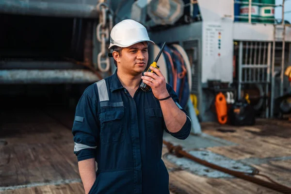 Marine Deck Officer o Chief mate en la cubierta de un buque o buque en alta mar, con equipo de protección personal del PPE casco, sobretodo. Sostiene radio VHF walkie-talkie en las manos. — Foto de Stock