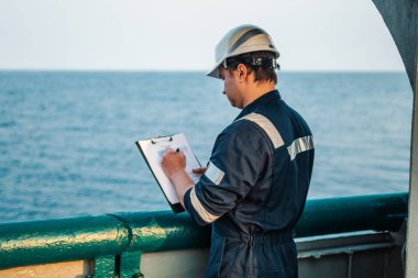 Güverte görevlisi offshore gemi veya gemi güvertede, PPE kişisel koruyucu ekipman giyiyor. Kontrol listesini doldurur. Denizdeki evraklar