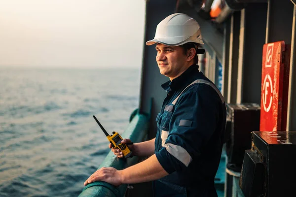 Denizci güvertesi subayı ya da kıyı gemisinin güvertesinde kaptan yardımcısı, PPE kişisel koruyucu ekipman giyiyorlar - miğfer, tulum. Elinde VHF telsizi var..