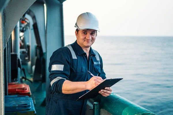 Oficial de convés no convés de embarcação ou navio offshore, usando equipamento de proteção individual EPI. Ele preenche a lista de verificação. Papelada no mar — Fotografia de Stock