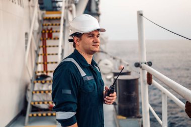 Denizci güvertesi subayı ya da kıyı gemisinin güvertesinde kaptan yardımcısı, PPE kişisel koruyucu ekipman giyiyorlar - miğfer, tulum. Elinde VHF telsizi var..