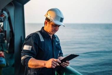 Güverte görevlisi offshore gemi veya gemi güvertede, PPE kişisel koruyucu ekipman giyiyor. Kontrol listesini doldurur. Denizdeki evraklar